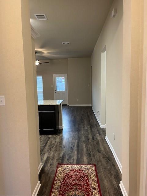 hallway featuring visible vents, dark wood finished floors, and baseboards