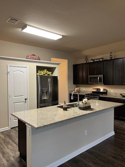 kitchen with a center island with sink, visible vents, dark wood finished floors, appliances with stainless steel finishes, and a sink