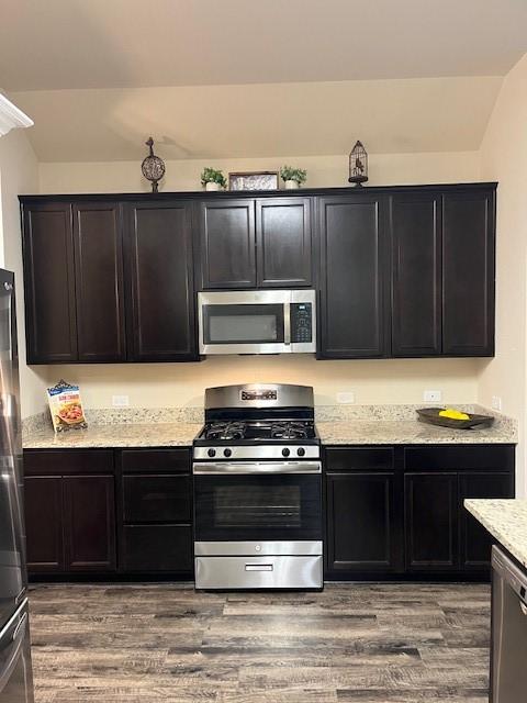 kitchen with stainless steel appliances, vaulted ceiling, light stone counters, and wood finished floors