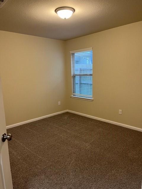 spare room featuring baseboards, dark carpet, and a textured ceiling