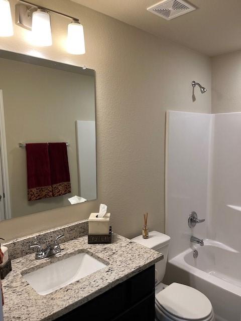 bathroom featuring visible vents, a textured wall, toilet, shower / bathtub combination, and vanity