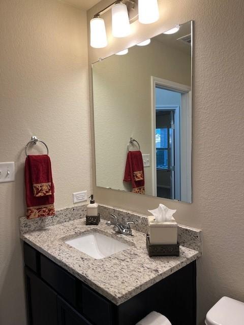 half bath featuring toilet, a textured wall, and vanity