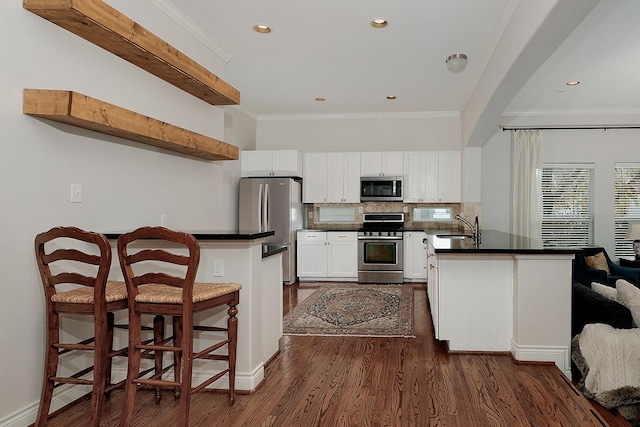 kitchen with sink, dark wood-type flooring, a breakfast bar area, white cabinets, and appliances with stainless steel finishes