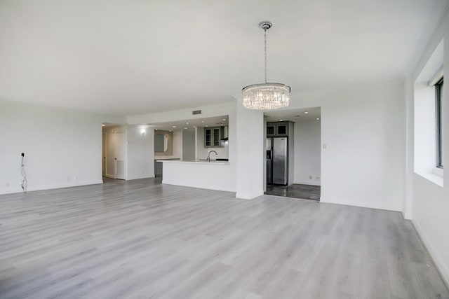 unfurnished living room with sink, light hardwood / wood-style flooring, and a chandelier