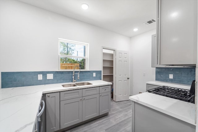 kitchen featuring light stone countertops, sink, backsplash, light hardwood / wood-style floors, and gray cabinets