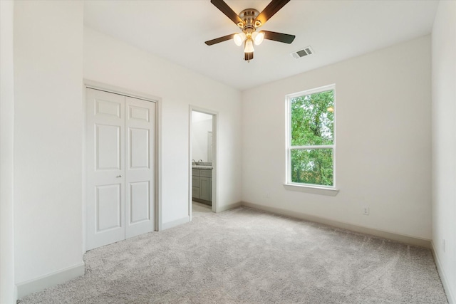 unfurnished bedroom with ensuite bath, ceiling fan, a closet, and light carpet