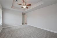 carpeted empty room with ceiling fan and a tray ceiling