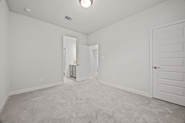 unfurnished bedroom with ensuite bathroom and light colored carpet