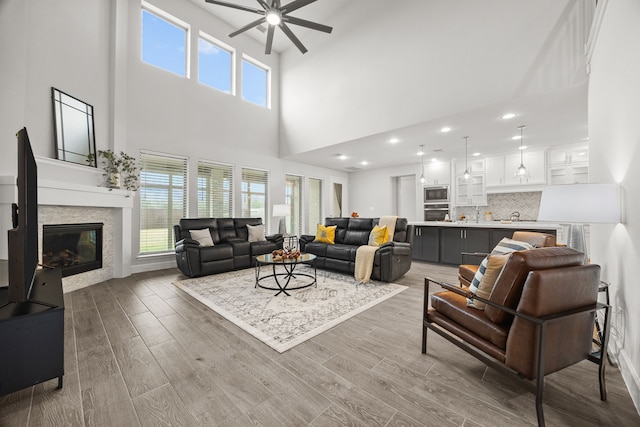 living room featuring a towering ceiling, a stone fireplace, ceiling fan, and sink