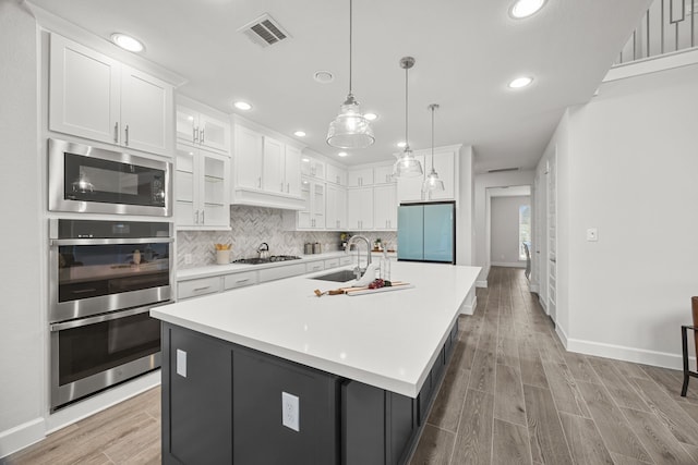 kitchen featuring appliances with stainless steel finishes, sink, a center island with sink, decorative light fixtures, and white cabinets