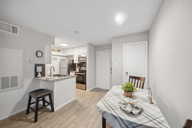 kitchen featuring sink, white cabinetry, light hardwood / wood-style floors, kitchen peninsula, and stainless steel appliances