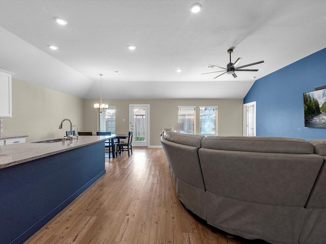 living room with ceiling fan with notable chandelier, sink, light hardwood / wood-style flooring, vaulted ceiling, and a textured ceiling