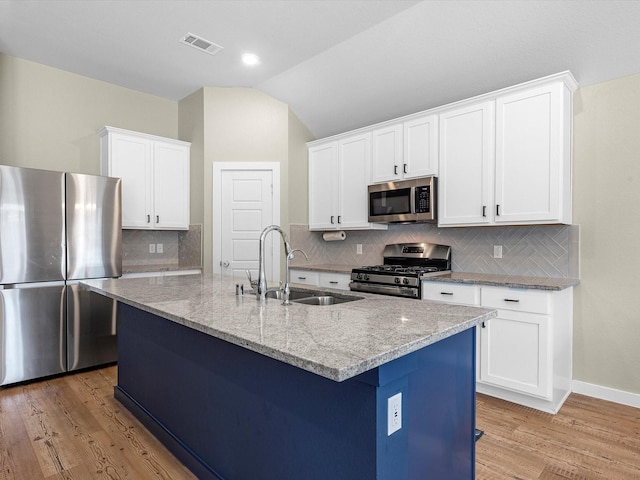 kitchen with lofted ceiling, a center island with sink, sink, light stone counters, and stainless steel appliances