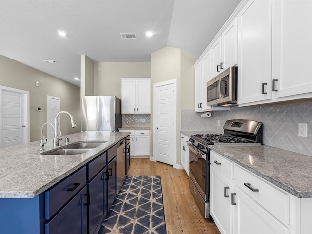 kitchen with appliances with stainless steel finishes, blue cabinets, sink, white cabinetry, and an island with sink