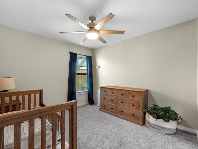 bedroom featuring light carpet, a nursery area, and ceiling fan