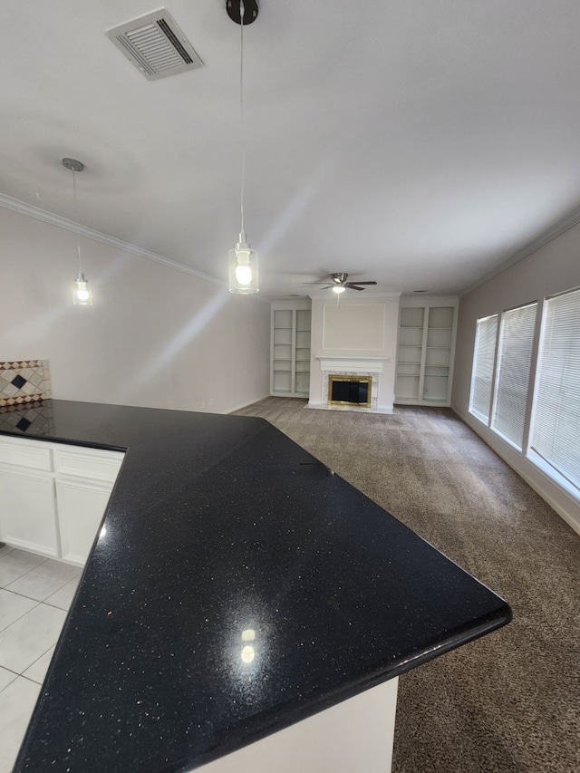 unfurnished living room featuring light carpet, built in shelves, ceiling fan, and crown molding