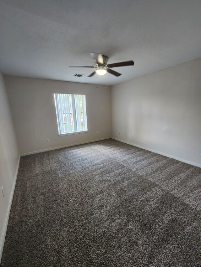 empty room featuring ceiling fan and dark carpet