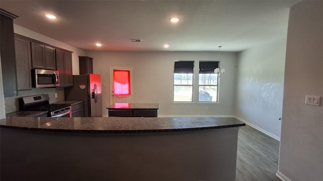 kitchen with kitchen peninsula, appliances with stainless steel finishes, backsplash, dark brown cabinetry, and wood-type flooring