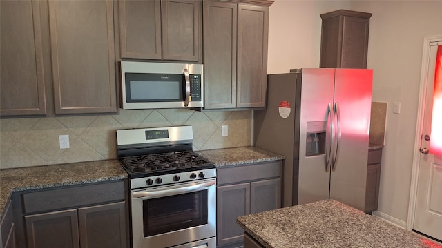 kitchen with dark stone countertops, dark brown cabinetry, backsplash, and appliances with stainless steel finishes