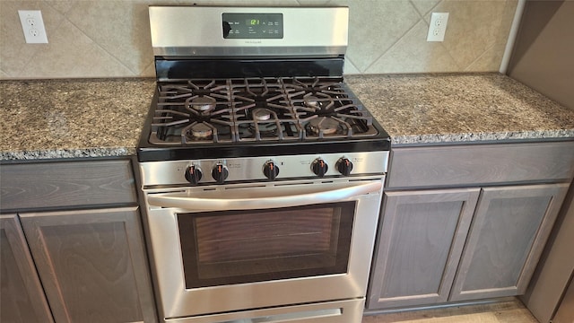 kitchen with decorative backsplash, dark stone countertops, and stainless steel gas range