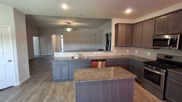 kitchen with a center island, sink, light hardwood / wood-style flooring, light stone countertops, and appliances with stainless steel finishes