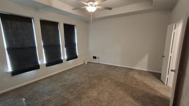 carpeted empty room featuring ceiling fan and a raised ceiling