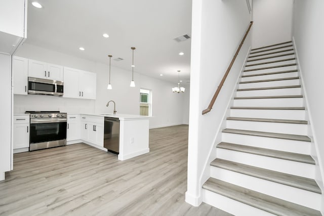 kitchen featuring kitchen peninsula, white cabinetry, decorative light fixtures, and appliances with stainless steel finishes