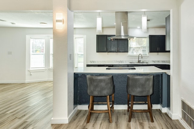 kitchen featuring sink, light hardwood / wood-style flooring, island exhaust hood, decorative light fixtures, and a breakfast bar