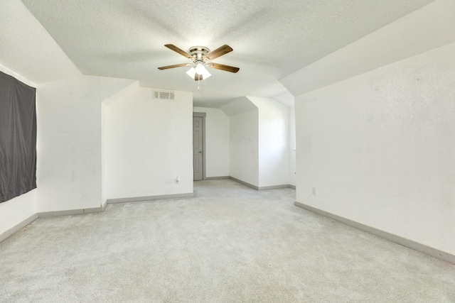 empty room with a textured ceiling, ceiling fan, light carpet, and vaulted ceiling