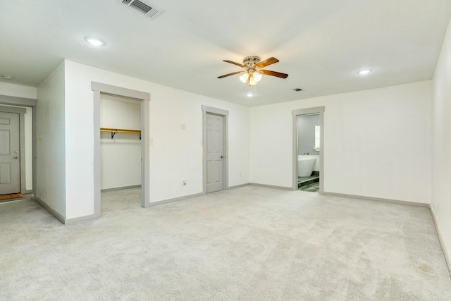 unfurnished bedroom featuring ensuite bathroom, a walk in closet, ceiling fan, light colored carpet, and a closet