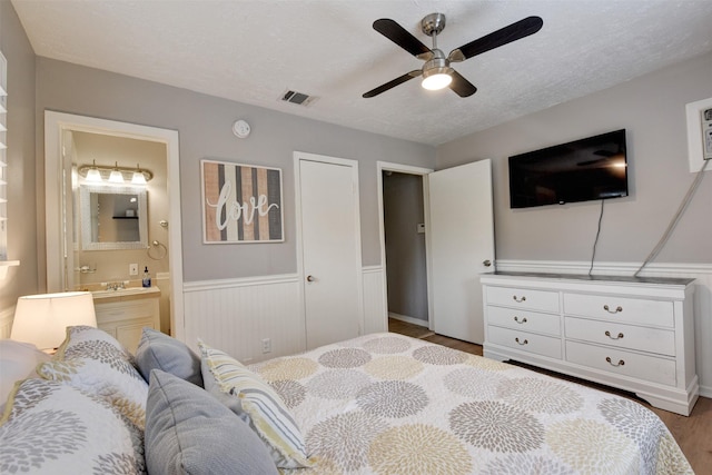 bedroom with a textured ceiling, ensuite bathroom, ceiling fan, and hardwood / wood-style flooring