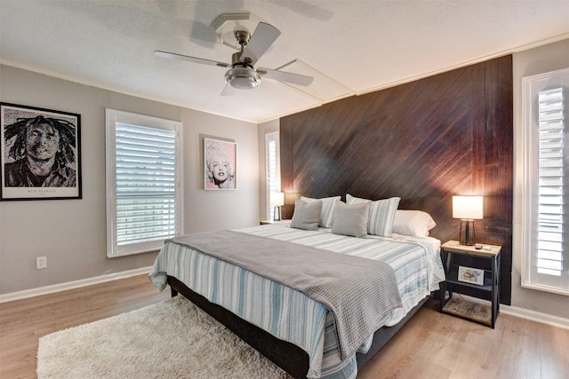 bedroom featuring multiple windows, light hardwood / wood-style flooring, ceiling fan, and wooden walls