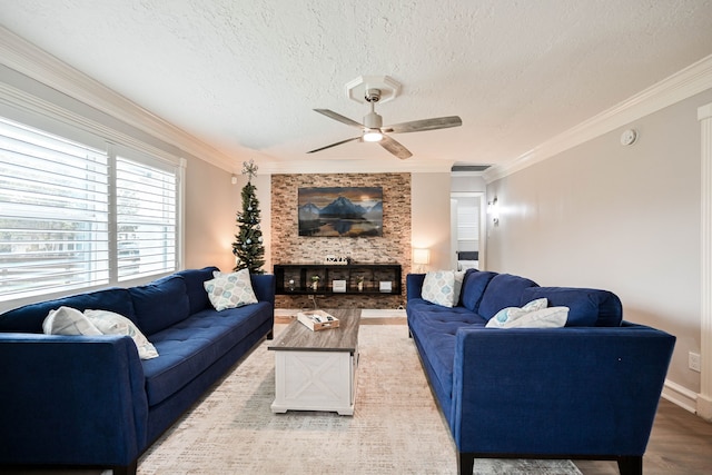 living room featuring a large fireplace, ceiling fan, ornamental molding, light wood-style floors, and a textured ceiling