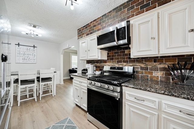 kitchen featuring appliances with stainless steel finishes, white cabinetry, and dark stone counters