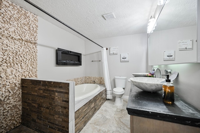 bathroom with tiled tub, vanity, a textured ceiling, and toilet