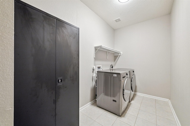 clothes washing area featuring light tile patterned floors, a textured ceiling, and separate washer and dryer