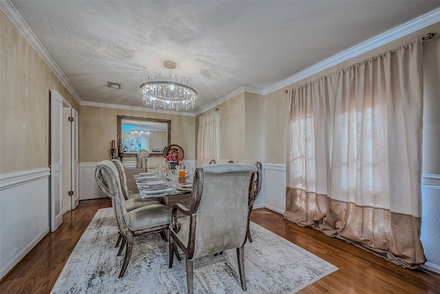 dining room with wood-type flooring, a textured ceiling, ornamental molding, and a notable chandelier