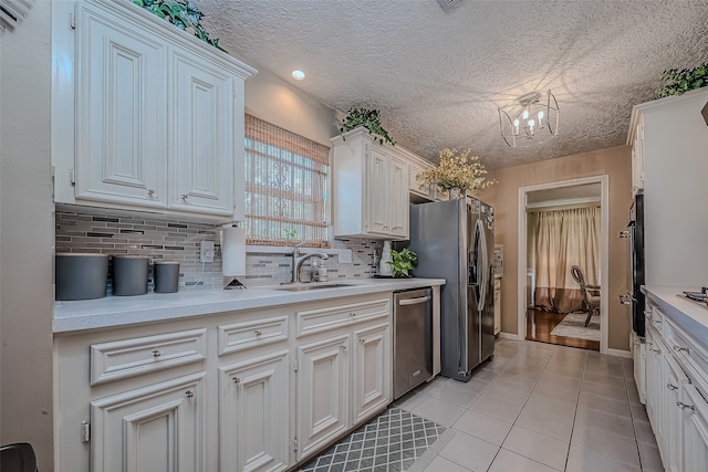 kitchen with sink, stainless steel appliances, light tile patterned floors, a chandelier, and white cabinets