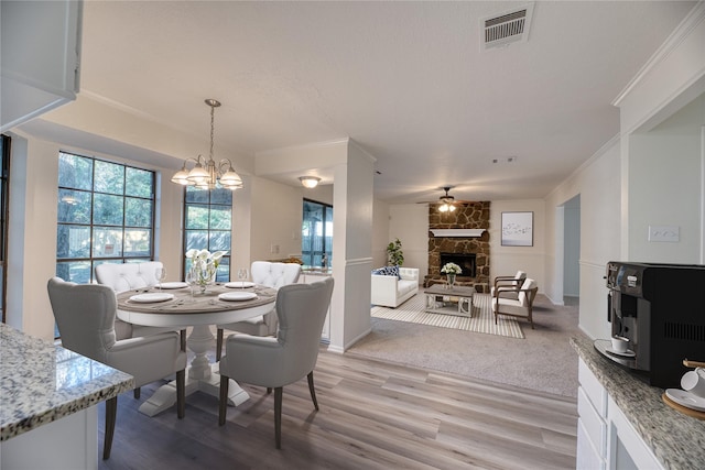 dining space featuring a fireplace, ceiling fan with notable chandelier, light hardwood / wood-style flooring, and ornamental molding