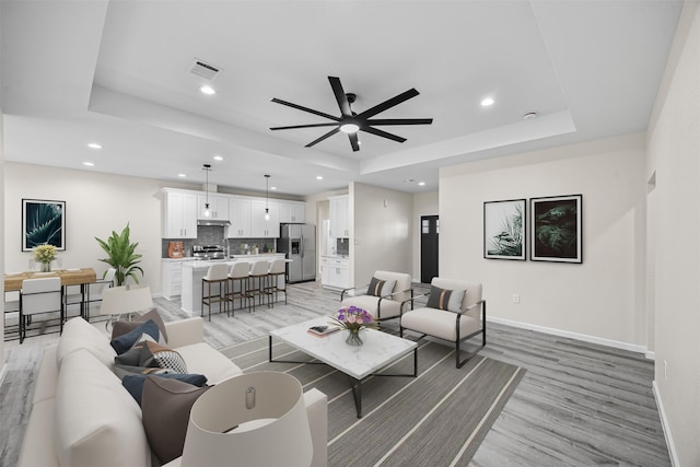 living room featuring a raised ceiling, ceiling fan, and light hardwood / wood-style flooring