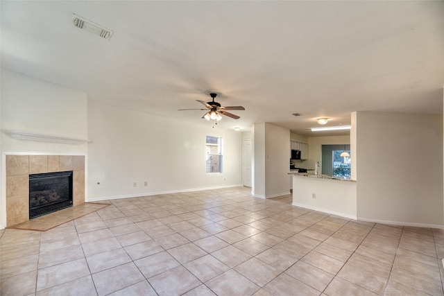 unfurnished living room with ceiling fan, a fireplace, light tile patterned flooring, and sink