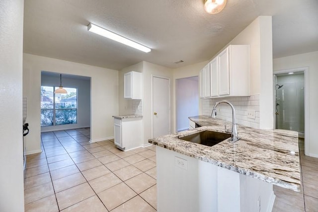 kitchen with light stone countertops, sink, backsplash, kitchen peninsula, and white cabinets