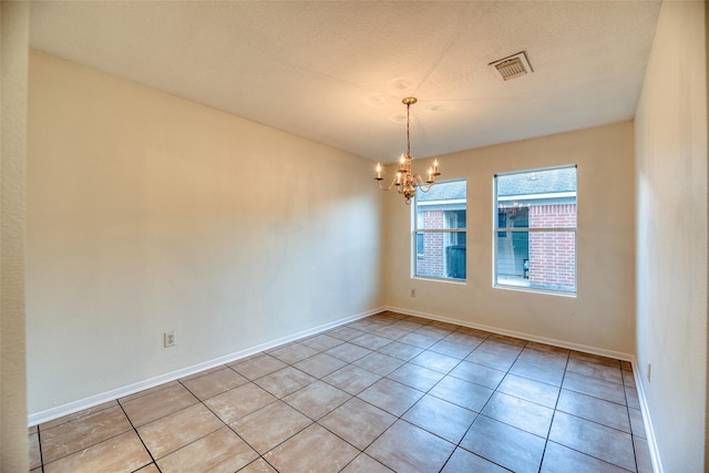 empty room with light tile patterned flooring and a chandelier