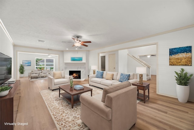 living room with a fireplace, light hardwood / wood-style floors, ceiling fan, and ornamental molding