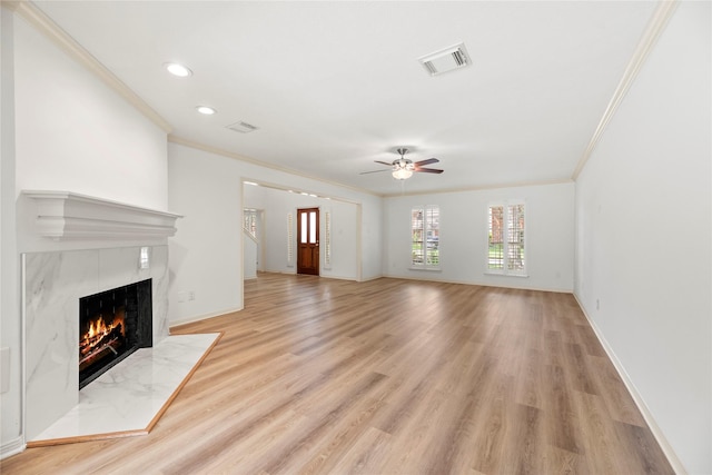 unfurnished living room featuring a tiled fireplace, ceiling fan, light hardwood / wood-style floors, and ornamental molding