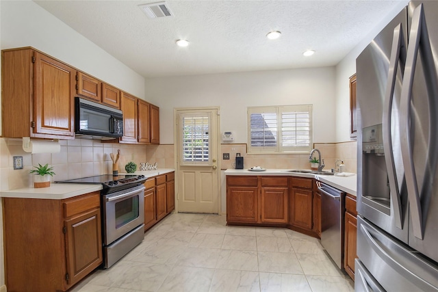 kitchen featuring a textured ceiling, stainless steel appliances, tasteful backsplash, and sink