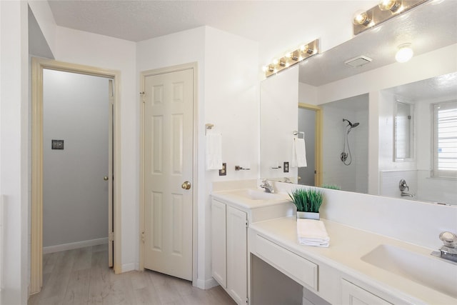 bathroom with hardwood / wood-style floors, vanity, tiled shower, and a textured ceiling