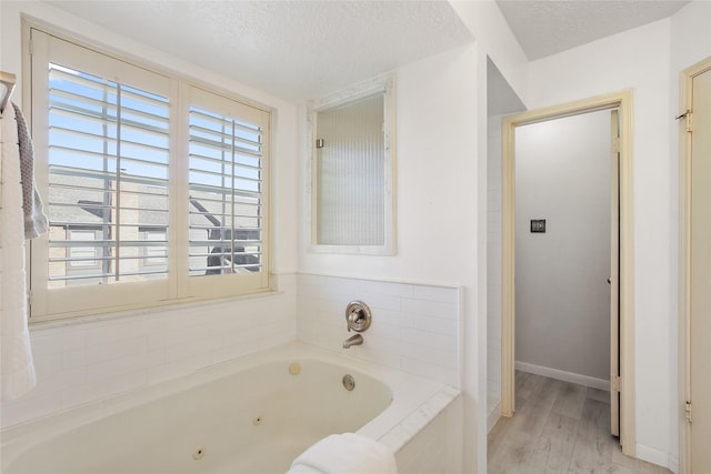 bathroom with hardwood / wood-style floors, a textured ceiling, and tiled tub