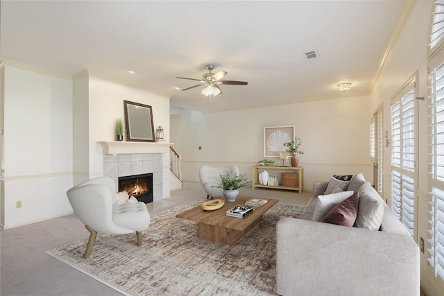 carpeted living room featuring ceiling fan, crown molding, and a tiled fireplace