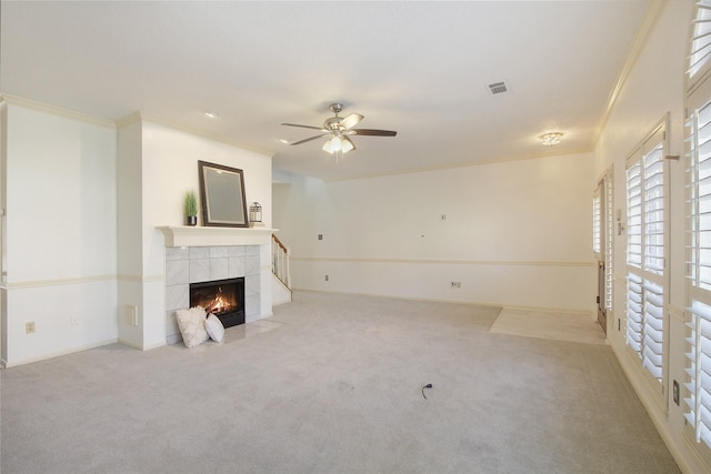 unfurnished living room featuring a tiled fireplace, ceiling fan, light carpet, and ornamental molding